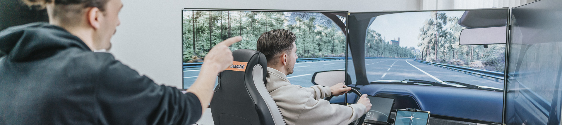 Fahrsimulator am Campus der Universität zu Lübeck: Studierende am Steuer einer virtuellen Fahrzeugkabine vor großen Monitoren